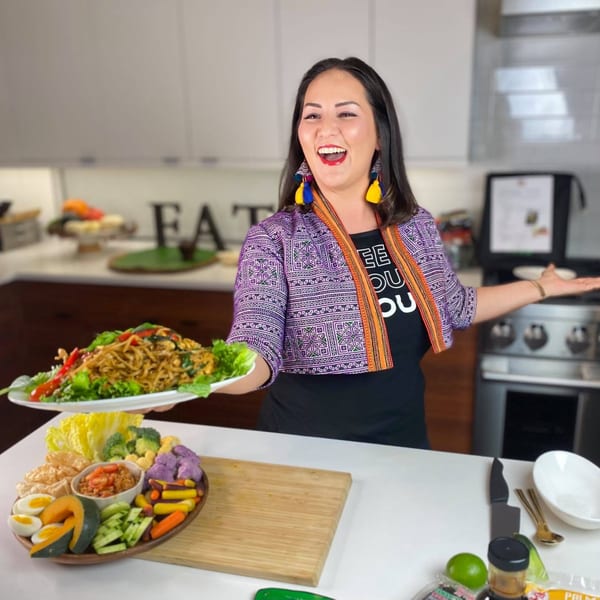 Chef Nikky from Asian Mint holding a plate of Thai noodles, with a vegetable platter on the counter.
