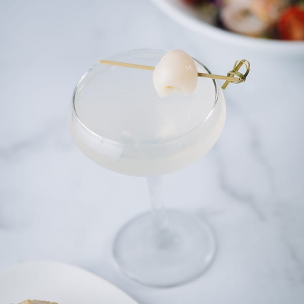 Lychee martini in a coupe glass, garnished with a lychee on a bamboo skewer.