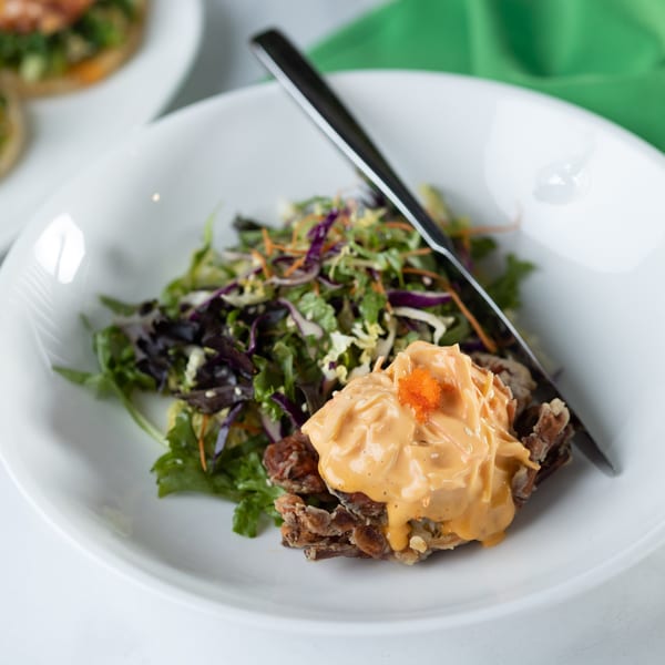 Crispy soft-shell crab topped with orange sauce and roe, served with a side salad.