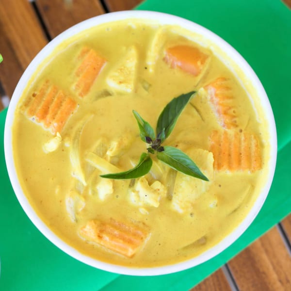 Overhead view of yellow Thai curry with carrots, chicken, and basil in a white bowl.
