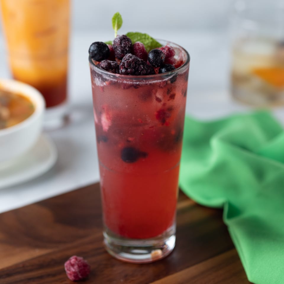 A vibrant red berry drink with mint garnish, alongside a Thai iced tea and a bowl of soup.