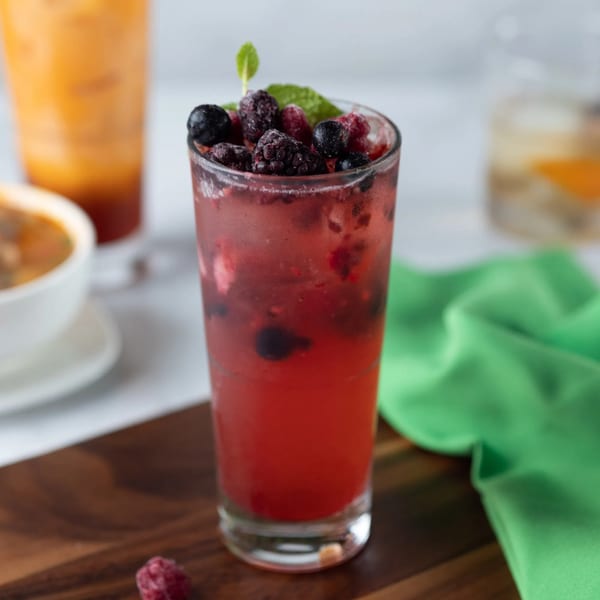 A refreshing berry cocktail with mint garnish, next to a Thai iced tea and soup.