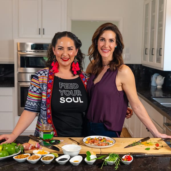 Two women in a kitchen with Thai ingredients and a dish on a cutting board.