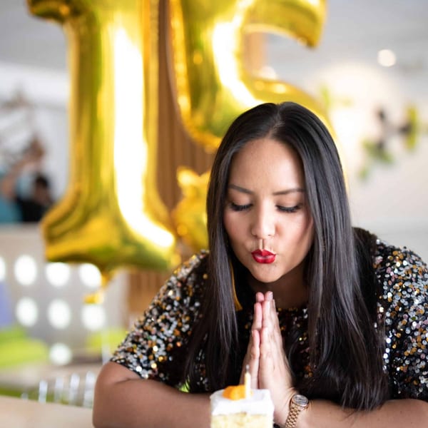 A woman in a sequined top blows out a candle on a small cake at Asian Mint.