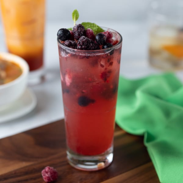 A vibrant red berry drink with mint and frosted berries, next to a green napkin on a wooden board.