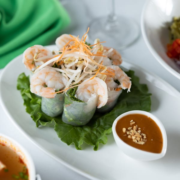 Fresh Thai spring rolls with shrimp, vegetables, and peanut sauce on a white plate.