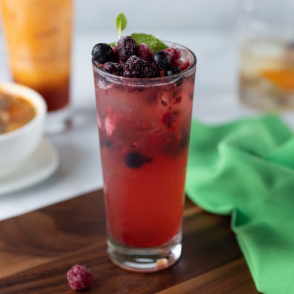 A vibrant red berry drink with mint garnish, alongside a Thai iced tea and a bowl of soup.