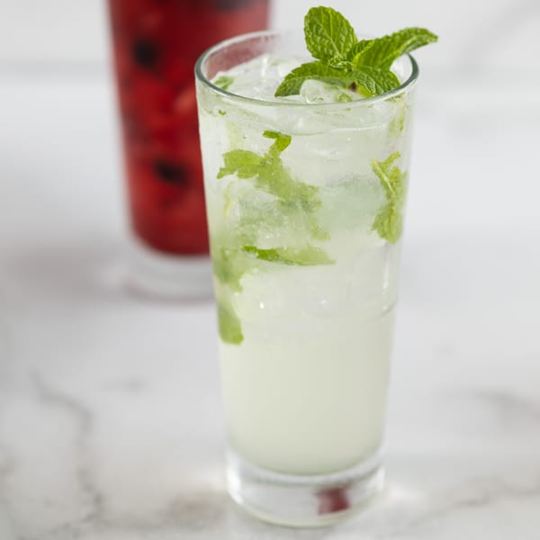 Refreshing mojito with mint leaves and ice, with a blurred red drink in the background.