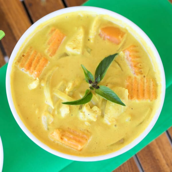 A bowl of yellow Thai curry with carrots, chicken, and basil on a green placemat.