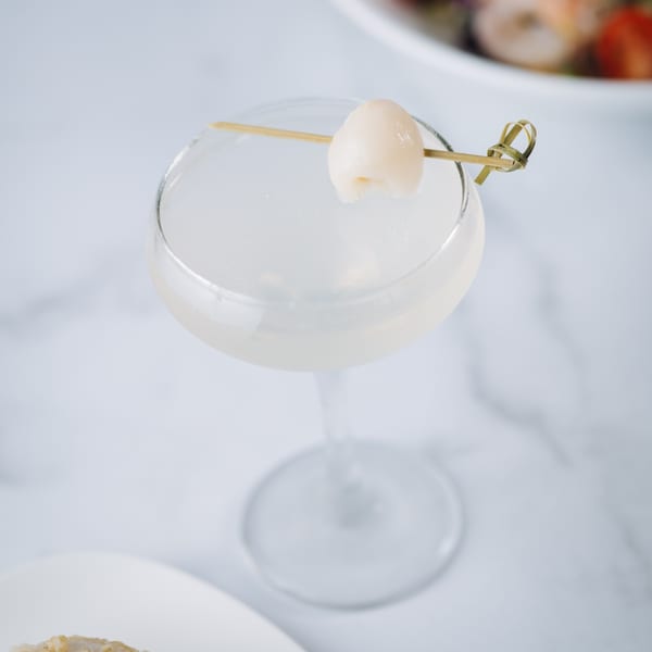 A lychee martini in a coupe glass, garnished with a single lychee on a skewer.