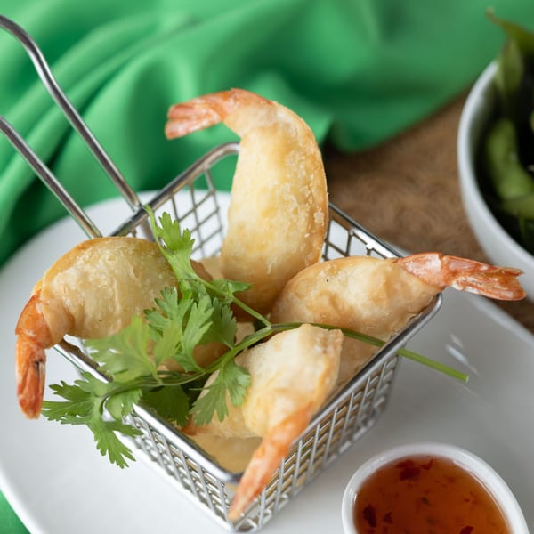 Crispy fried shrimp with cilantro in a metal basket, served with a sweet chili dipping sauce.