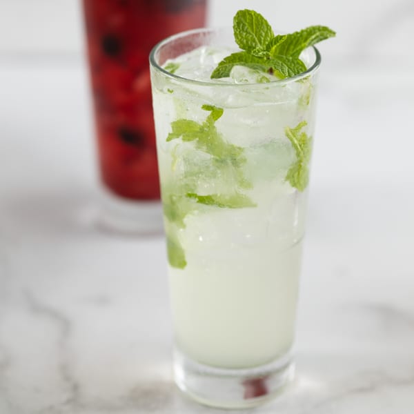 A refreshing mint mojito with ice, garnished with fresh mint leaves, next to a red drink.