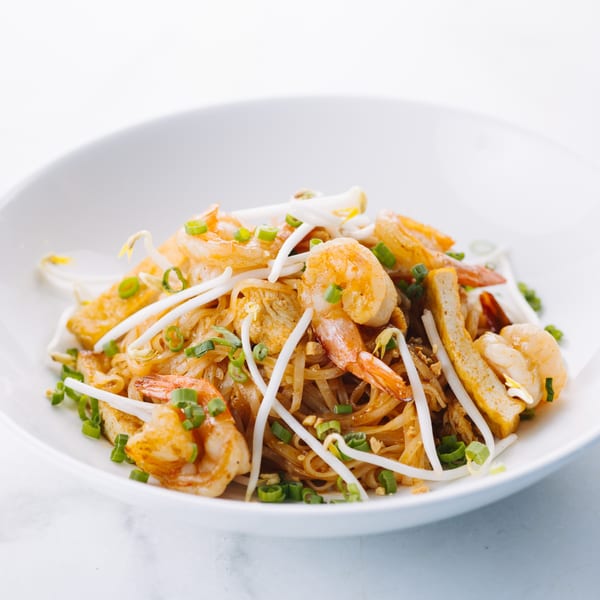 A white bowl filled with Thai Pad See Ew noodles, shrimp, bean sprouts, and green onions.