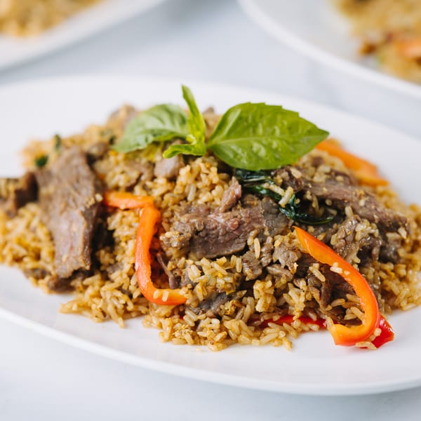 Thai basil fried rice with beef, red bell peppers, and fresh basil on a white plate.