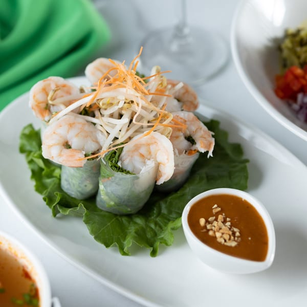 Fresh Thai shrimp spring rolls with bean sprouts, carrots, and peanut sauce on a white plate.