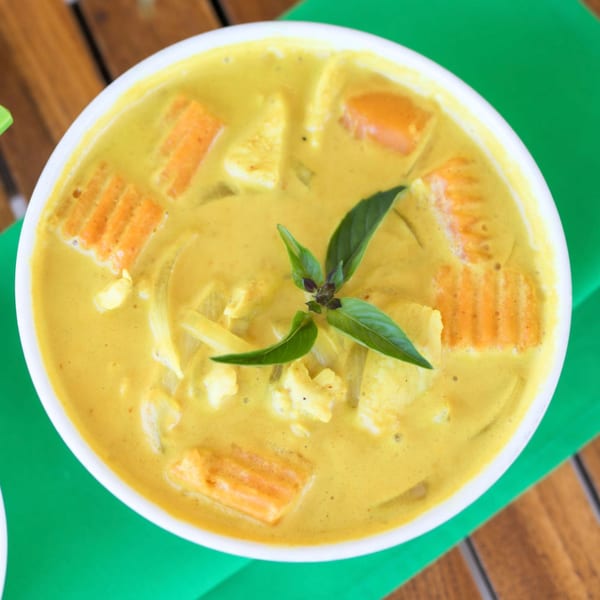 A white bowl of yellow Thai curry with chicken, carrots, and basil on a green placemat.