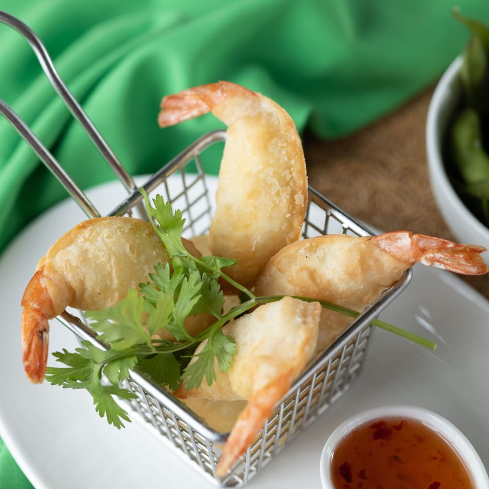 Crispy fried shrimp with cilantro in a metal basket, served with a sweet chili dipping sauce.