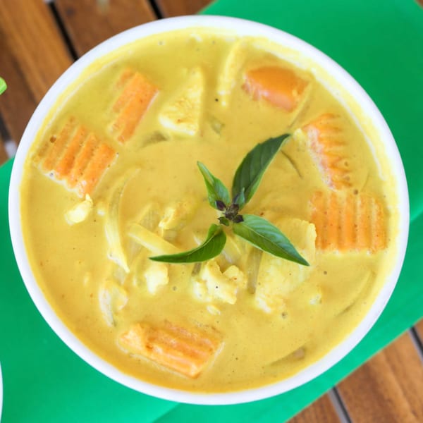 Close-up of a bowl of yellow Thai curry with chicken, carrots, and basil on a green placemat.