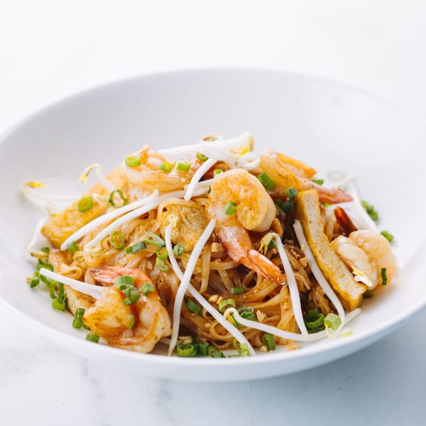 Close-up of a white bowl filled with shrimp pad Thai, garnished with bean sprouts and green onions.