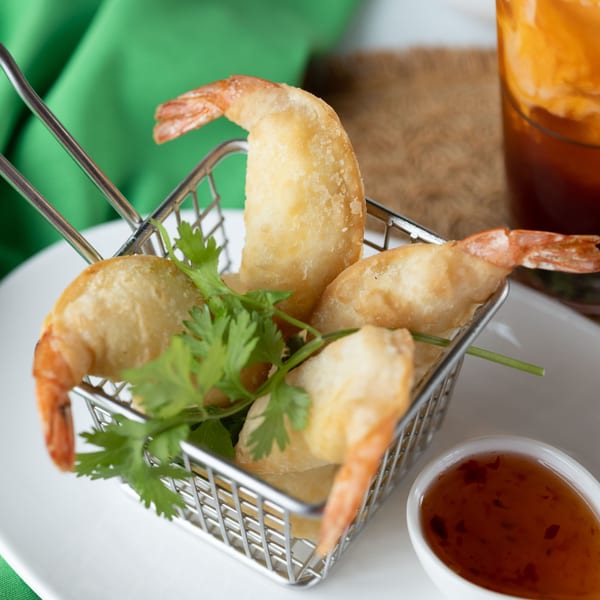 Crispy fried shrimp with cilantro in a metal basket, served with sweet chili sauce.