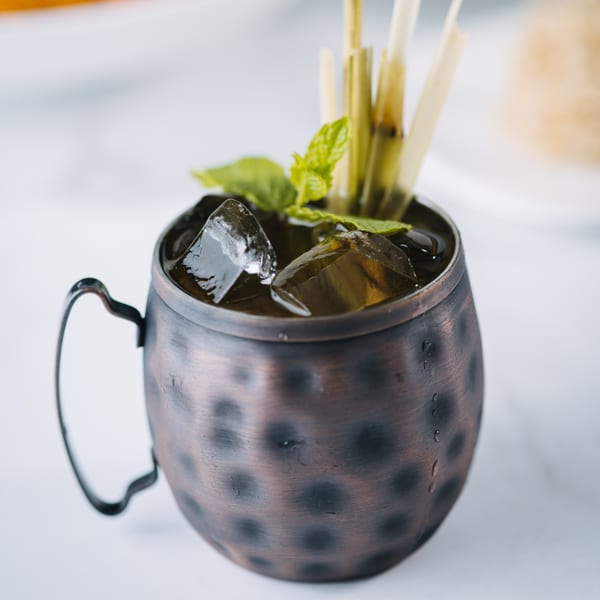 A Thai iced tea in a hammered copper mug with ice, mint, and lemongrass garnish.