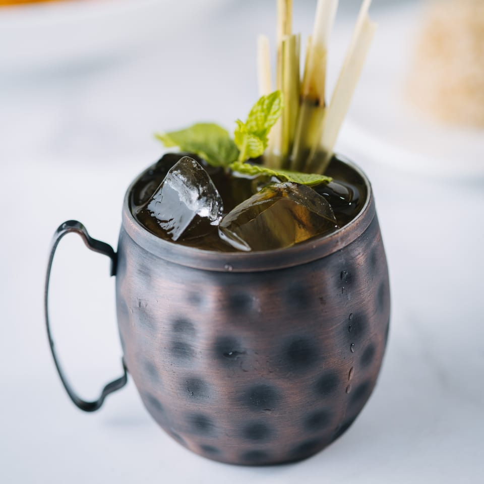 Iced Thai drink in a hammered copper mug, garnished with mint and lemongrass.