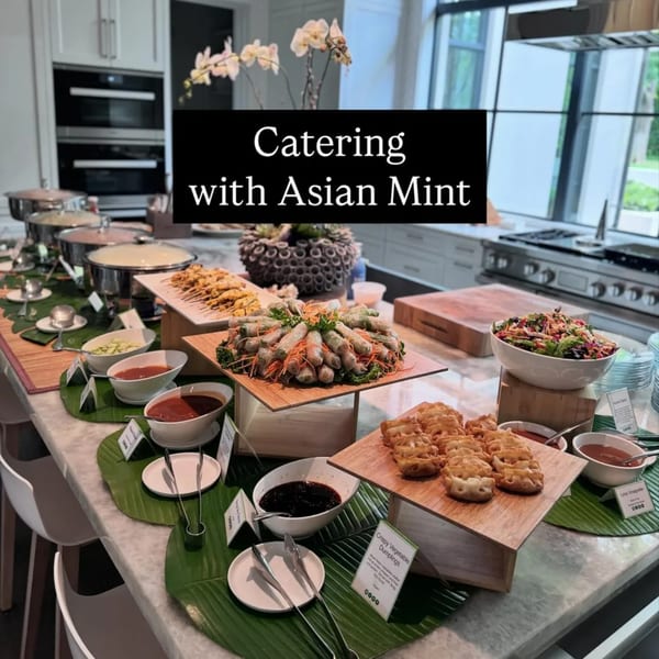 A buffet table filled with various Thai dishes, including spring rolls, dumplings, and satay.