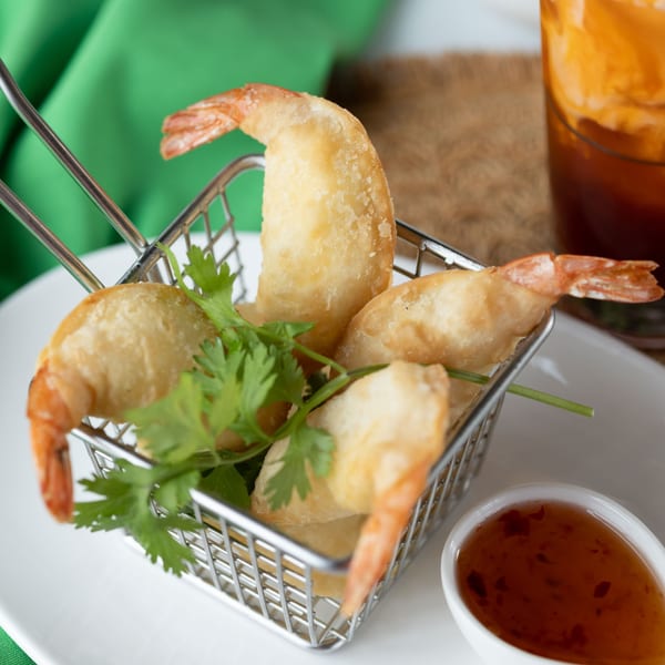Crispy fried shrimp with cilantro in a metal basket, served with a side of sweet chili sauce.