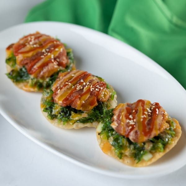 Three crispy Thai appetizers topped with green seaweed salad, orange sauce, and sesame seeds.