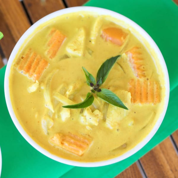Close-up of a bowl of yellow Thai curry with carrots, chicken, and basil on a green placemat.