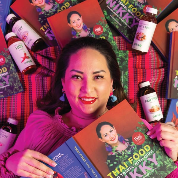 Chef Nikky smiles, surrounded by her Thai cookbooks and bottles of Asian Mint sauces.