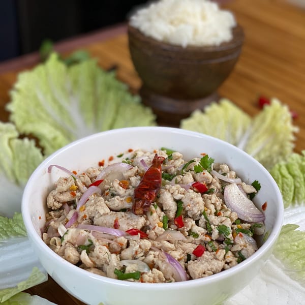 A white bowl of Thai Larb Gai with lettuce wraps and a wooden bowl of rice.