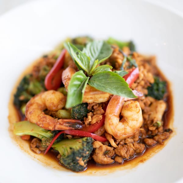Thai basil stir-fry with shrimp, chicken, broccoli, and red bell peppers in a white bowl.