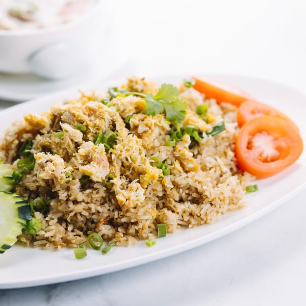 Thai crab fried rice with green onions, cilantro, cucumber, and tomato slices on a white plate.