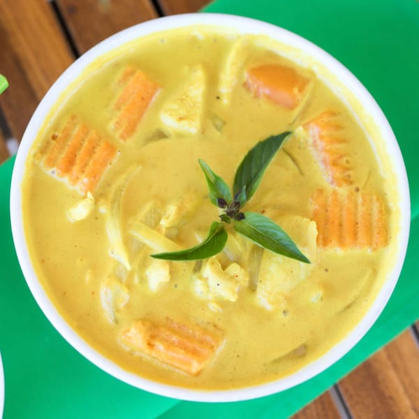 Overhead view of a bowl of yellow Thai curry with carrots, chicken, and basil.