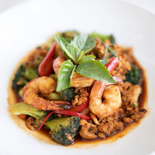 Thai basil stir-fry with shrimp, chicken, broccoli, and red bell peppers in a white bowl.