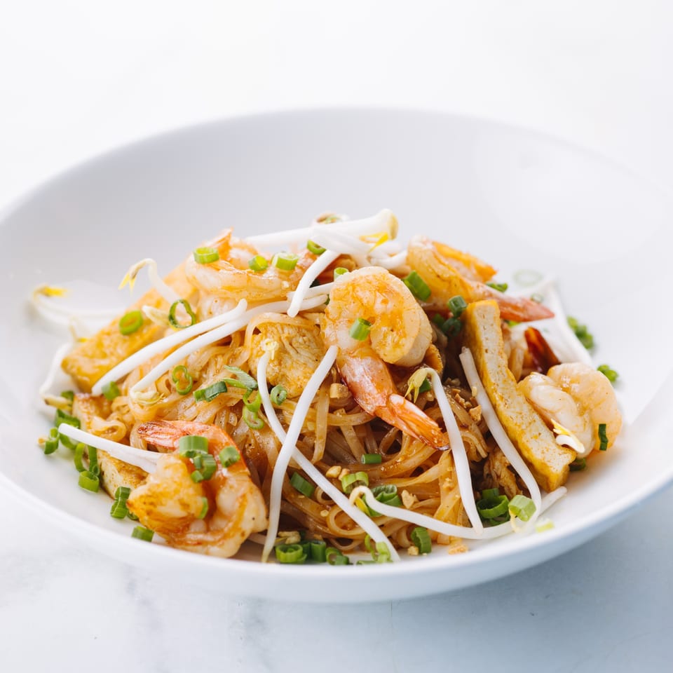 Close-up of a white bowl filled with Thai shrimp Pad See Ew noodles, bean sprouts, and green onions.