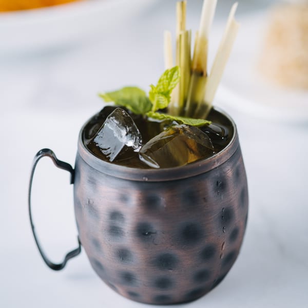 Iced Thai drink in a hammered copper mug, garnished with mint and lemongrass stalks.